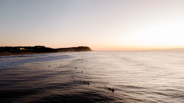 A watercolor painting of a serene Australian beach with surfers catching waves at sunset.