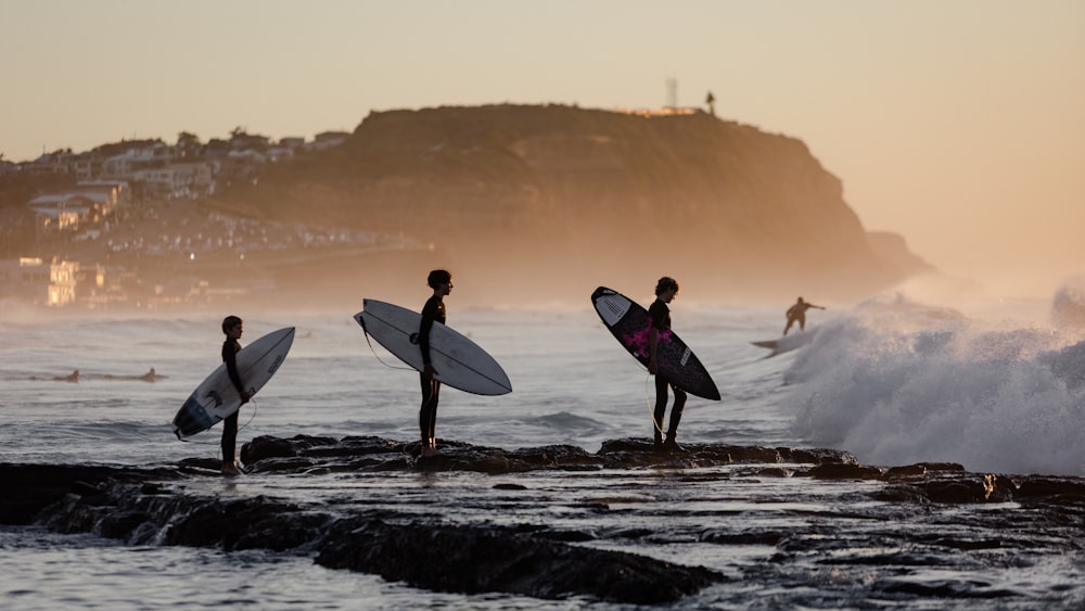 a group of people standing on top of a beach holding surfboards