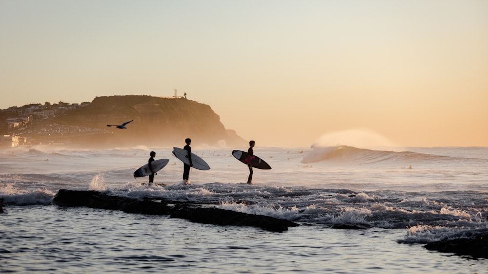 three surfers walking into the ocean with their surfboards