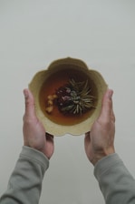 Hands holding a terracotta bowl filled with wholesome plant-based food, soft beige background.