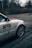 The image features a close-up of a white car with alloy wheels. The car has a prominent logo and text 'Harris' on the side, with a red and black design. It is parked on a paved area surrounded by bare trees, suggesting a cold, possibly winter, setting.