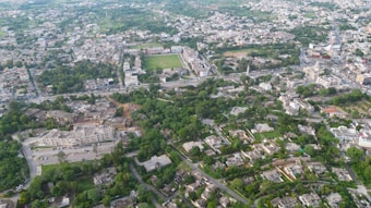 An aerial view of a city with numerous buildings, roads, and green patches, suggesting a mix of urban development and vegetation. The area contains a variety of residential and possibly commercial structures, including a few large complexes. The layout indicates a planned urban region with organized streets and blocks.