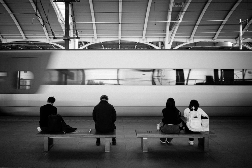 three people sitting on a bench in front of a train