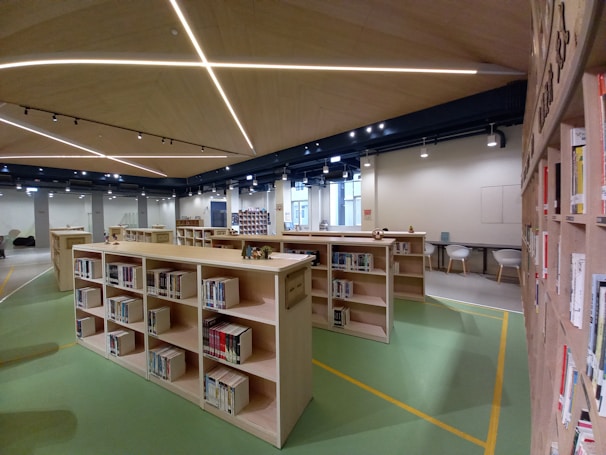 A bright, modern library interior with rows of bookshelves and students studying at wooden tables.