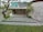 A modern architectural structure with concrete walls, an overhang, and a green roof. There are steps leading down to an entrance with glass doors labeled 'shop.' The surrounding landscape includes neatly trimmed grass and trees, providing a harmonious blend of nature and structure.
