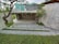 A modern architectural structure with concrete walls, an overhang, and a green roof. There are steps leading down to an entrance with glass doors labeled 'shop.' The surrounding landscape includes neatly trimmed grass and trees, providing a harmonious blend of nature and structure.