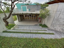 A modern architectural structure with concrete walls, an overhang, and a green roof. There are steps leading down to an entrance with glass doors labeled 'shop.' The surrounding landscape includes neatly trimmed grass and trees, providing a harmonious blend of nature and structure.