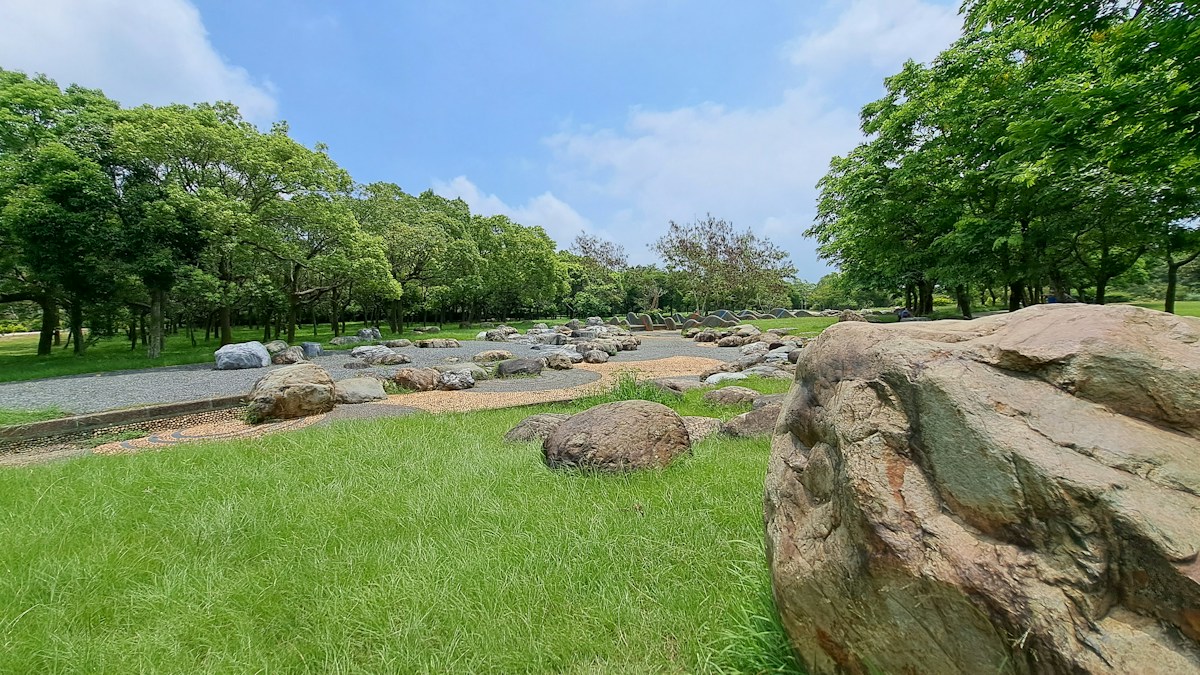 A wide lawn and stone garden path lined with trees in a Taiwanese city park