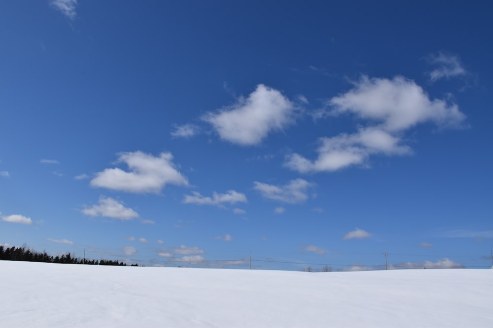a snow covered field under a blue sky with clouds