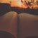 An open book with pages fluttering in the wind against a backdrop of a sunset.