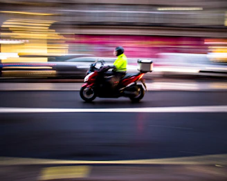 A Moto Flash rider in yellow and gold uniform navigating a narrow urban street on a sleek motorcycle.
