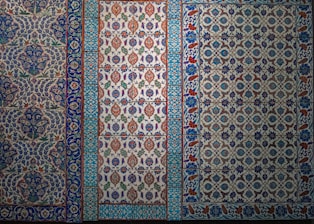 The image features a series of intricately designed tiles with intricate floral and geometric patterns. The tiles display a variety of colors, predominantly featuring blues, whites, reds, and greens with elaborate motifs and symmetrical designs.