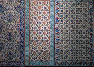 The image features a series of intricately designed tiles with intricate floral and geometric patterns. The tiles display a variety of colors, predominantly featuring blues, whites, reds, and greens with elaborate motifs and symmetrical designs.