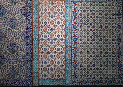 The image features a series of intricately designed tiles with intricate floral and geometric patterns. The tiles display a variety of colors, predominantly featuring blues, whites, reds, and greens with elaborate motifs and symmetrical designs.