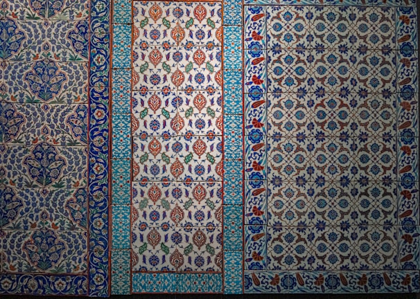 The image features a series of intricately designed tiles with intricate floral and geometric patterns. The tiles display a variety of colors, predominantly featuring blues, whites, reds, and greens with elaborate motifs and symmetrical designs.