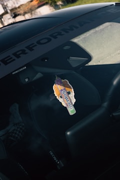 A car interior is shown with a focus on the sticker attached to the windshield. The sticker features colorful artwork and the word 'mentos' is prominently displayed. The interior includes a Recaro seat, and the word 'PERFORMANCE' is visible on the windshield's sunstrip.