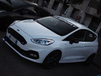 A pristine white BMW with M Sport alloy stickers perfectly aligned on each wheel, parked on a city street.