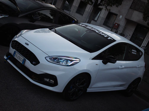 A pristine white BMW with M Sport alloy stickers perfectly aligned on each wheel, parked on a city street.