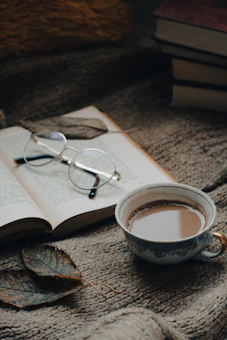 A cozy workspace with stacks of colorful books and a writer's notebook open beside a steaming cup of tea.