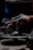 Hands covered in clay are intricately shaping a pottery piece on a rotating potter's wheel. The environment is dimly lit, highlighting the texture and detail of both the hands and the clay. The focus is on the creative process and craftsmanship involved in pottery making.