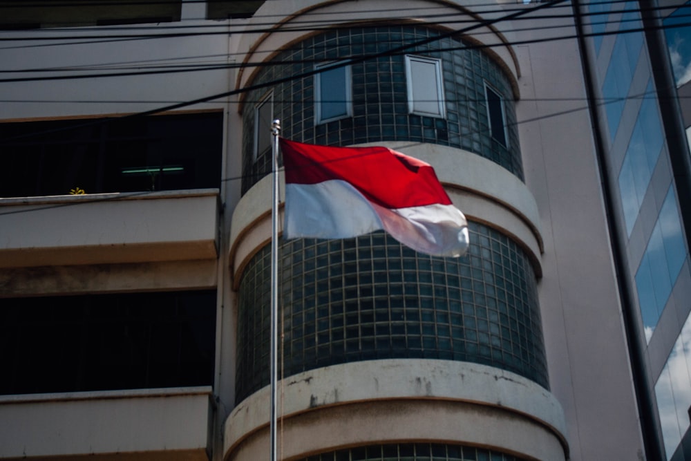 a red and white flag flying in front of a building