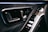 A close-up shot of a car interior, featuring a luxurious, modern design. It highlights the door panel with sleek silver handles and control buttons, complemented by stitched leather upholstery.