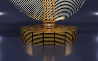 A futuristic, abstract design featuring a series of stacked golden disks forming a circular base. Rising from the center is a column of tightly coiled golden rings, with a large, swirling metallic structure resembling a helix or wave, hovering above. The image has a sleek, polished appearance with reflective surfaces and soft lighting.