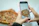 Smiling woman enjoying a slice of pizza at home with a smartphone nearby.
