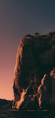 A shadowy ancient cliff bathed in golden and orange light under a twilight sky.