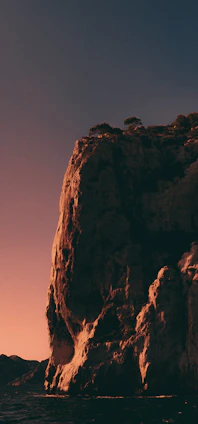 A shadowy ancient cliff bathed in golden and orange light under a twilight sky.