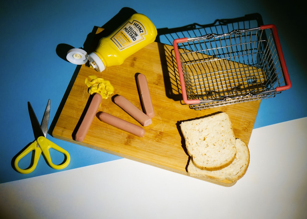 a cutting board with bread, mustard, butter, and a pair of scissors