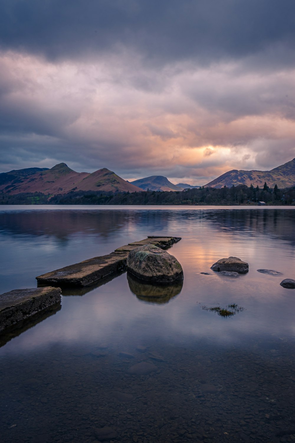 a body of water surrounded by mountains under a cloudy sky