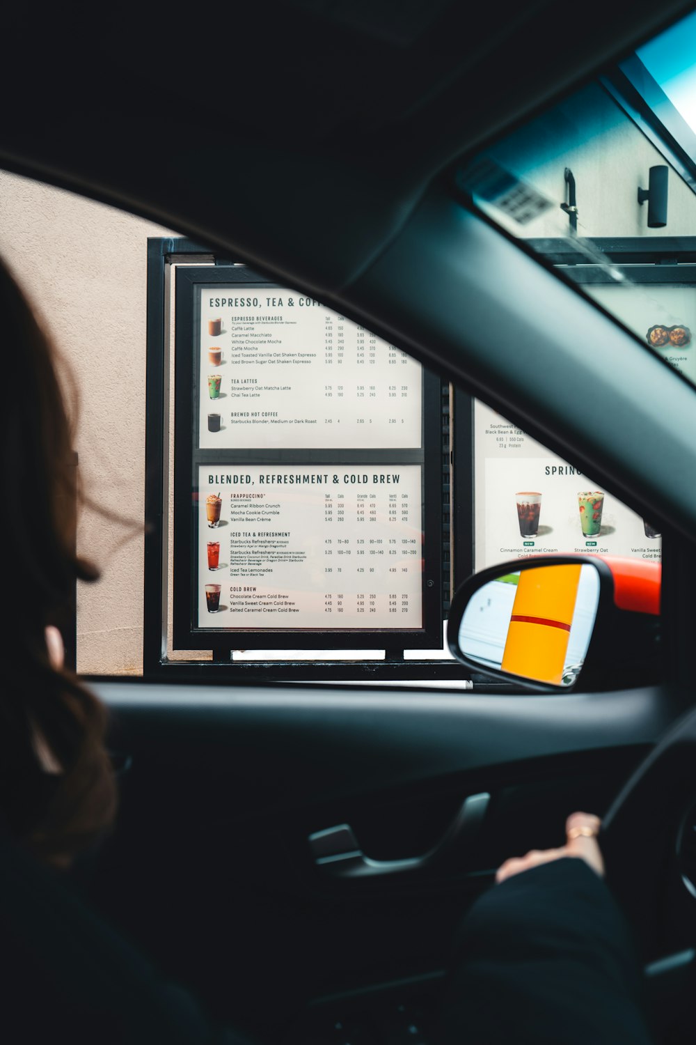 a woman driving a car past a menu board