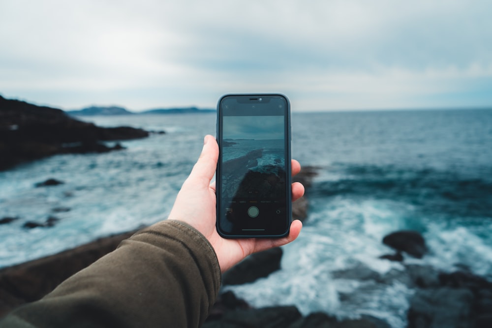 a person holding a cell phone in front of a body of water