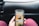 A person is holding a smartphone displaying a coffee shop app, showing an advertisement for cold brew coffee. The phone is held in front of a car dashboard. The background includes part of a steering wheel and the car's interior.