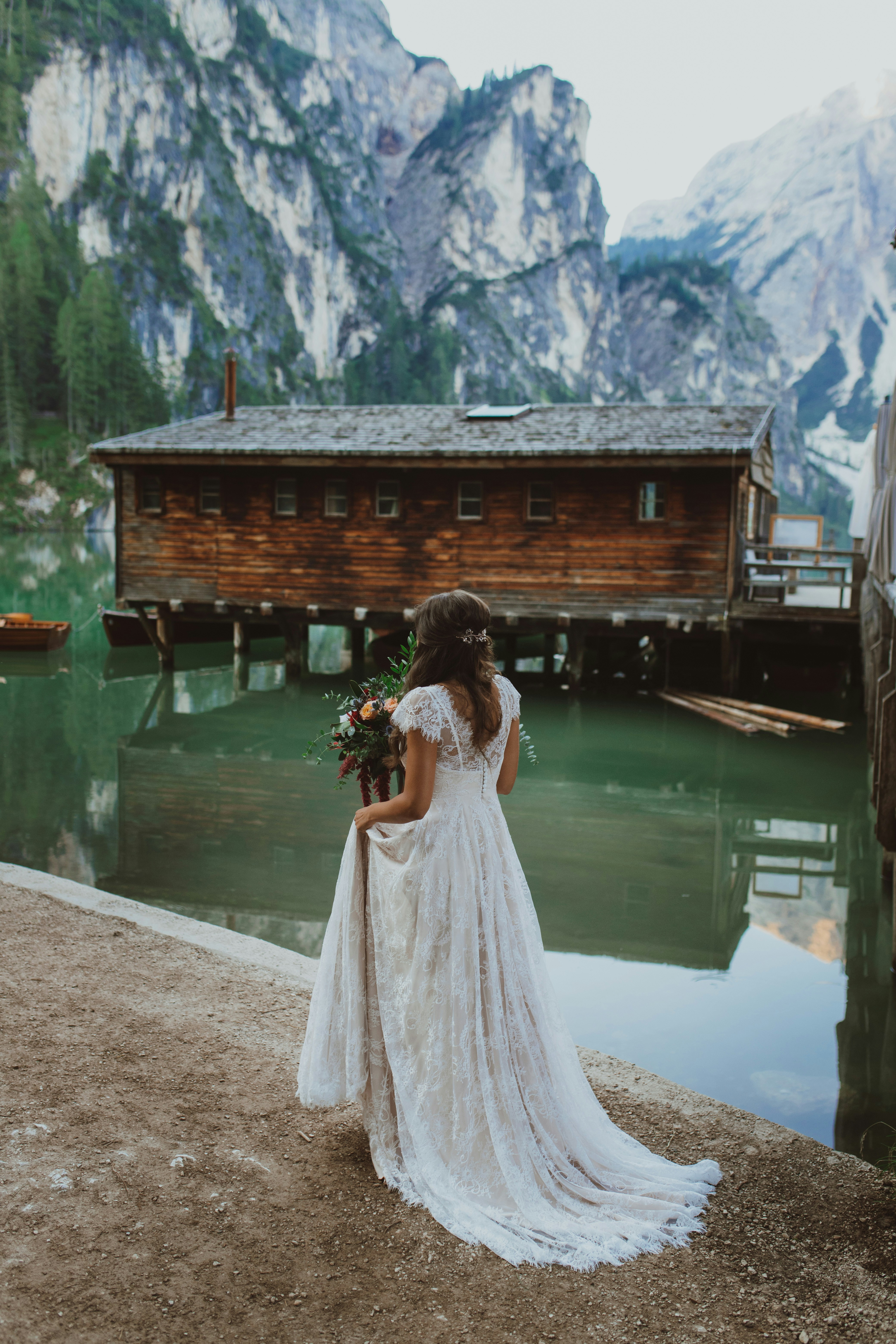 uma mulher em um vestido de noiva de pé ao lado de um lago
