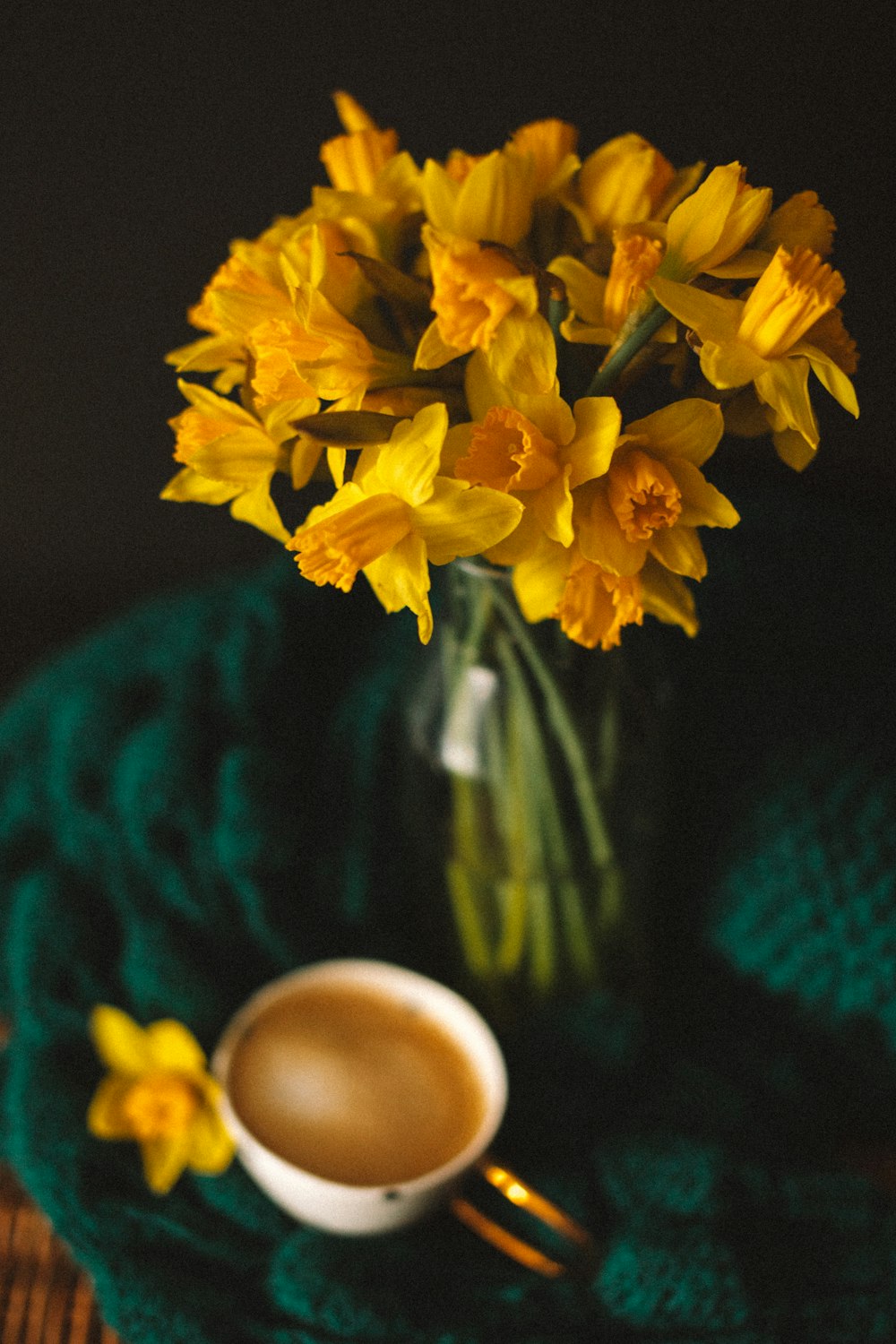 eine mit gelben Blumen gefüllte Glasvase neben einer Tasse Kaffee