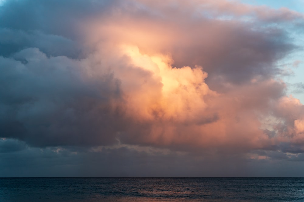 a large cloud hangs over the ocean as the sun sets
