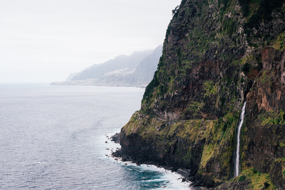 a waterfall is on the side of a cliff next to the ocean