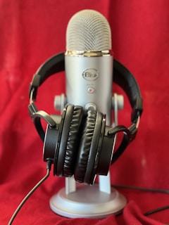 A silver microphone is standing on a base with a pair of black headphones draped over it. The background is a rich red fabric, which adds warmth to the scene.