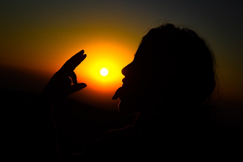 a silhouette of a person holding a cell phone in front of the sun