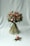 A beautifully arranged bouquet consisting of various flowers and greenery. The bouquet features pink roses, white daisies, and other floral elements, bound together neatly with long green leaves. It is accompanied by a smaller floral arrangement placed on a light grey background.