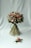 A beautifully arranged bouquet consisting of various flowers and greenery. The bouquet features pink roses, white daisies, and other floral elements, bound together neatly with long green leaves. It is accompanied by a smaller floral arrangement placed on a light grey background.