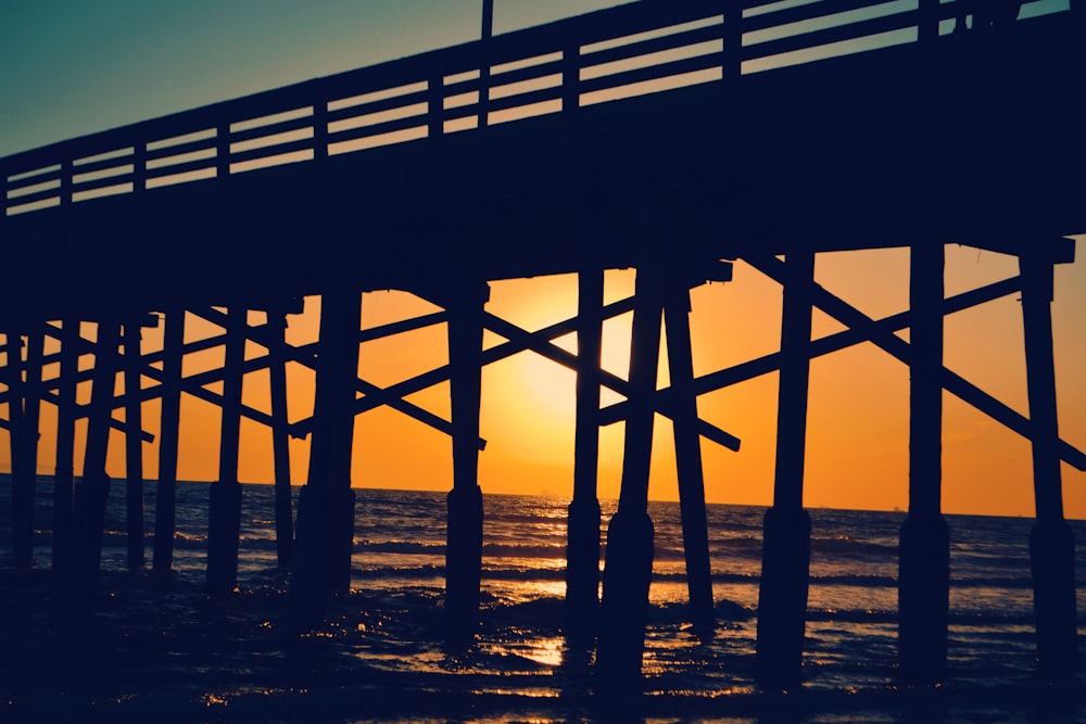 the sun is setting behind a pier on the water