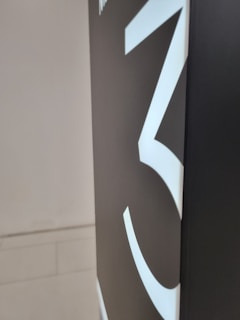 A large, bold white number three is displayed prominently on a dark background, likely part of a sign or artwork. The background is mostly a deep black or dark grey shade, contributing to a stark contrast with the number.