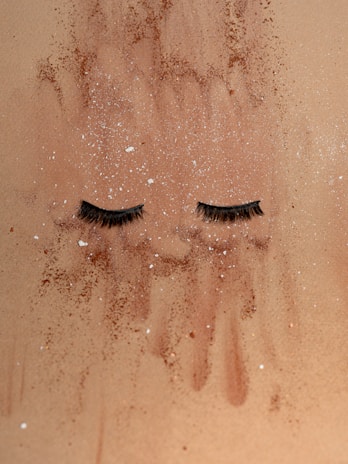False eyelashes are laid on a sandy surface dusted with specks of brown and white powder.