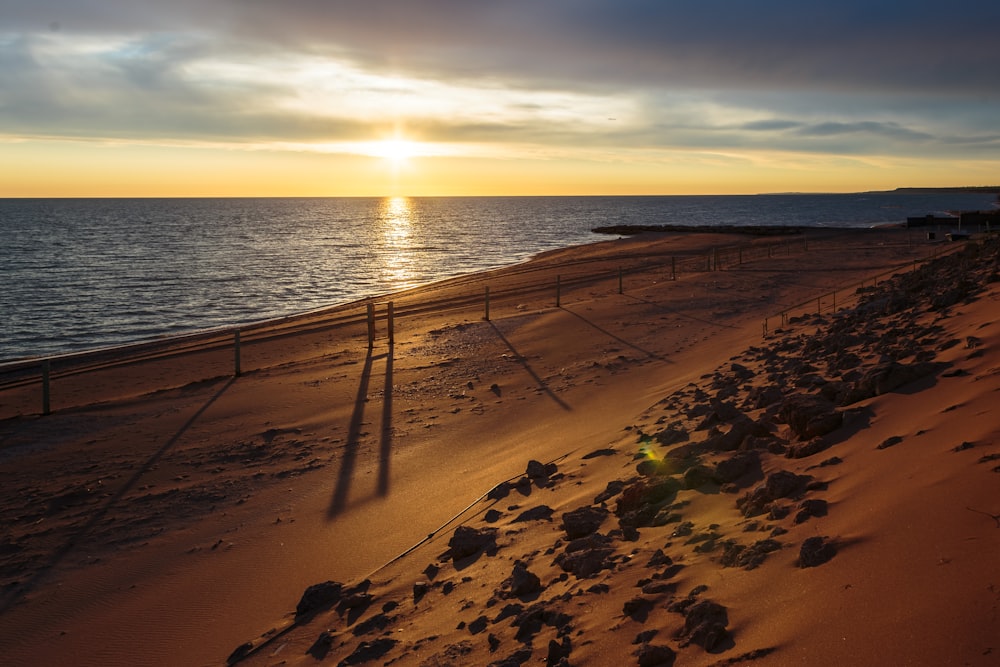 the sun is setting over the water on the beach