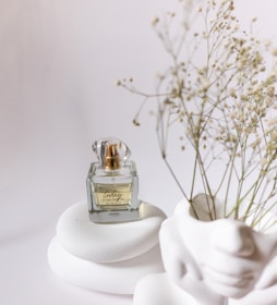 Elegant perfume bottle with dark glass and gold details on a minimalist white background.
