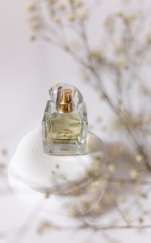 Close-up of a delicate glass bottle filled with golden attar oil, resting on a soft white fabric.