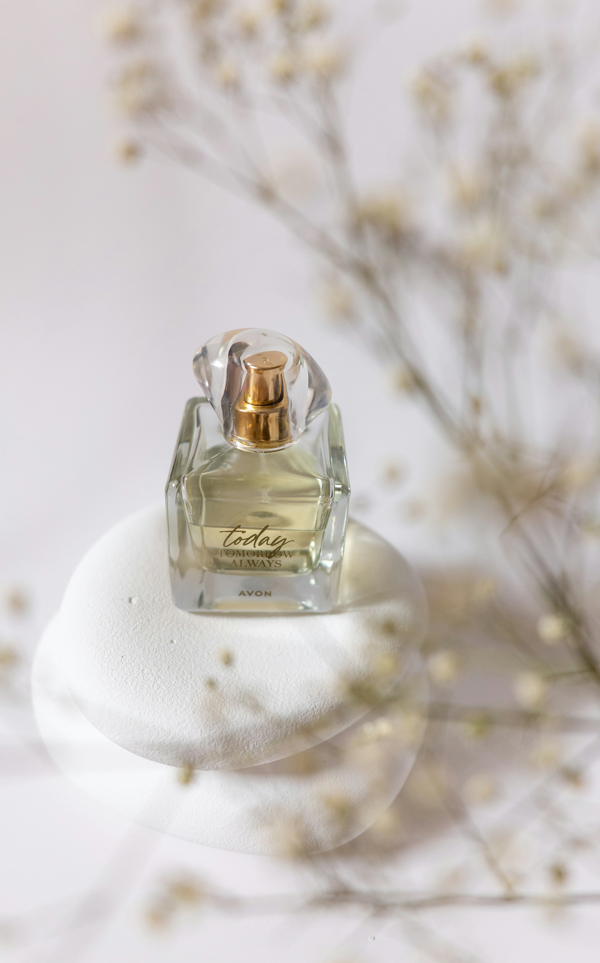 A serene close-up of a perfume bottle with white and gold accents, droplets of water glistening on its surface against a soft beige background.